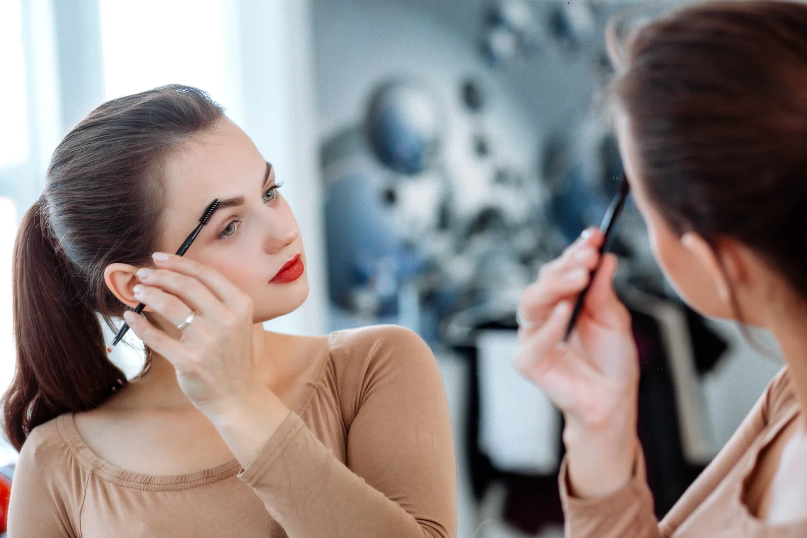 Vrouw bekijkt haar wenkbrauwen terwijl een stylist meekijkt.