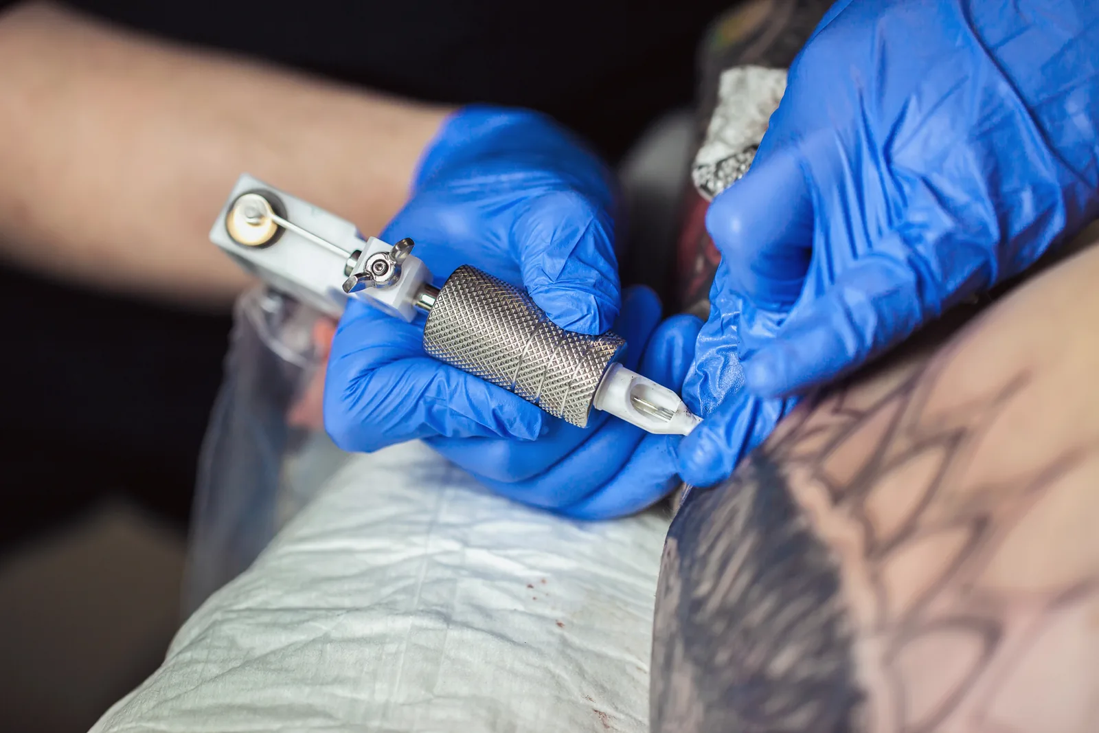 Tatoeëerder met blauwe handschoenen werkt met een tattoomachine.