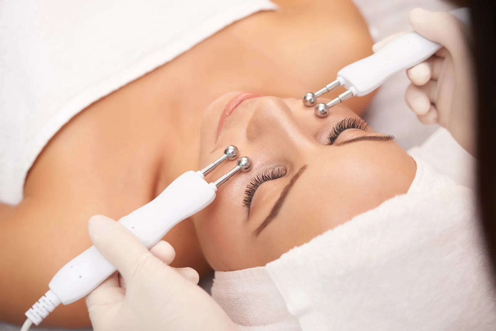 Vrouw ligt ontspannen met gesloten ogen tijdens een gezichtsverzorging in een salon.
