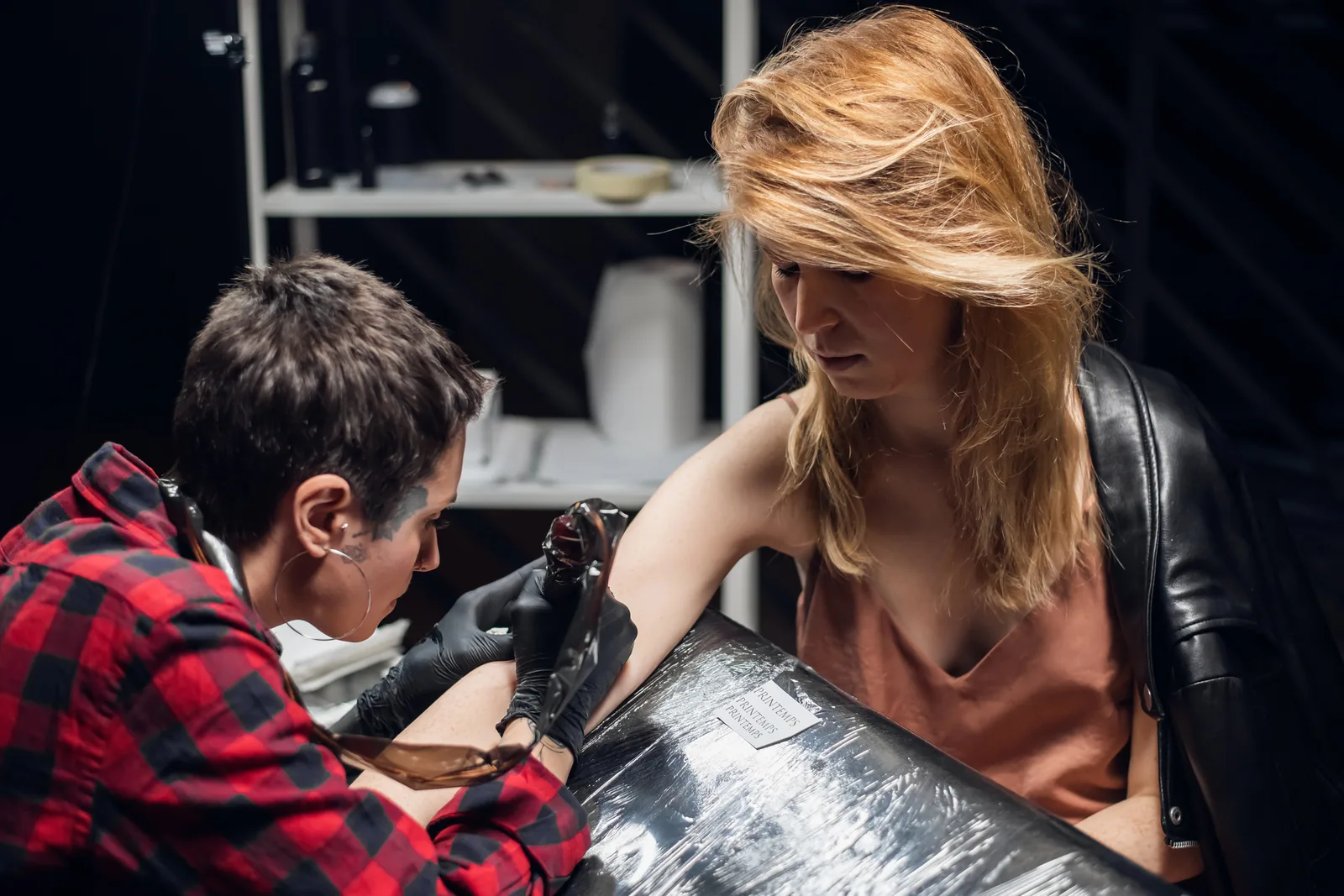 Tatoeëerder zet een tattoo op de arm van een jonge vrouw.