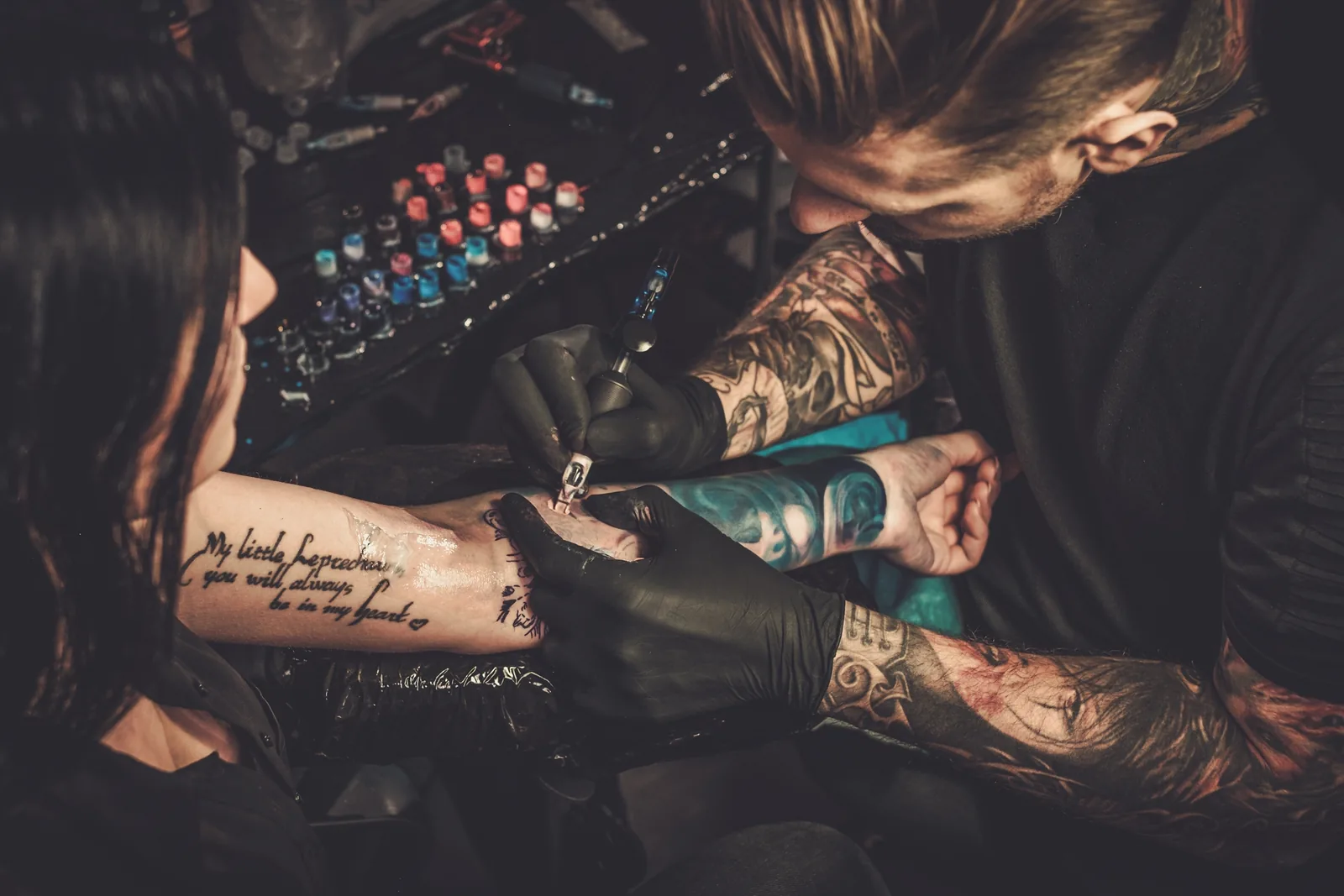 Tatoeëerder werkt aan een tattoo, met potjes inkt op de achtergrond.