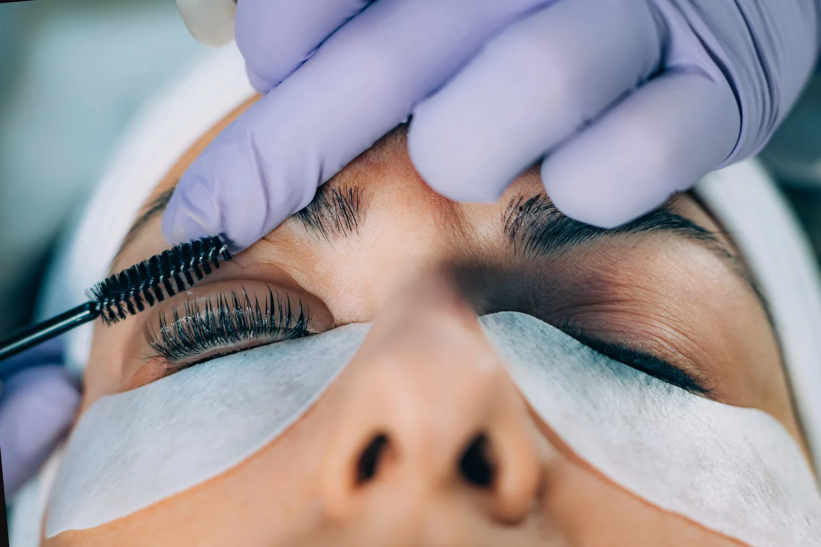 Wimpers worden met een borsteltje gekamd tijdens een lash lift, met een pad onder het oog.