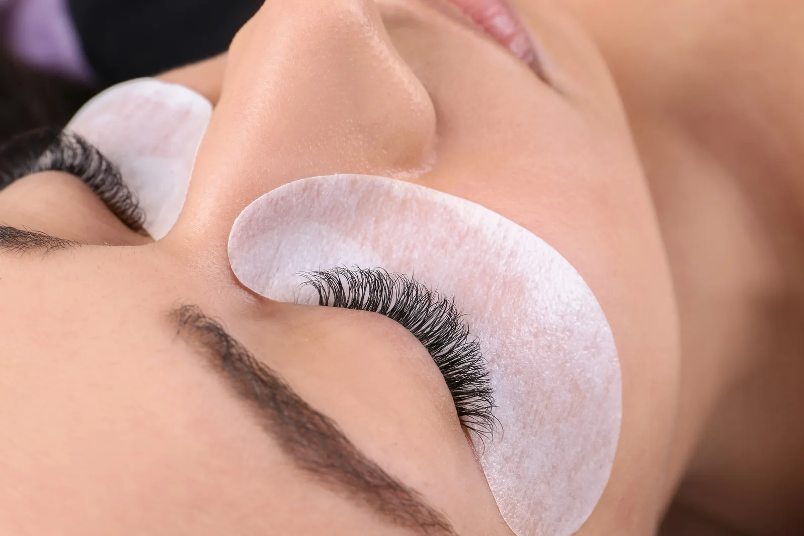 Close-up van een vrouw met wimperextensions en een pad onder het oog tijdens de behandeling.