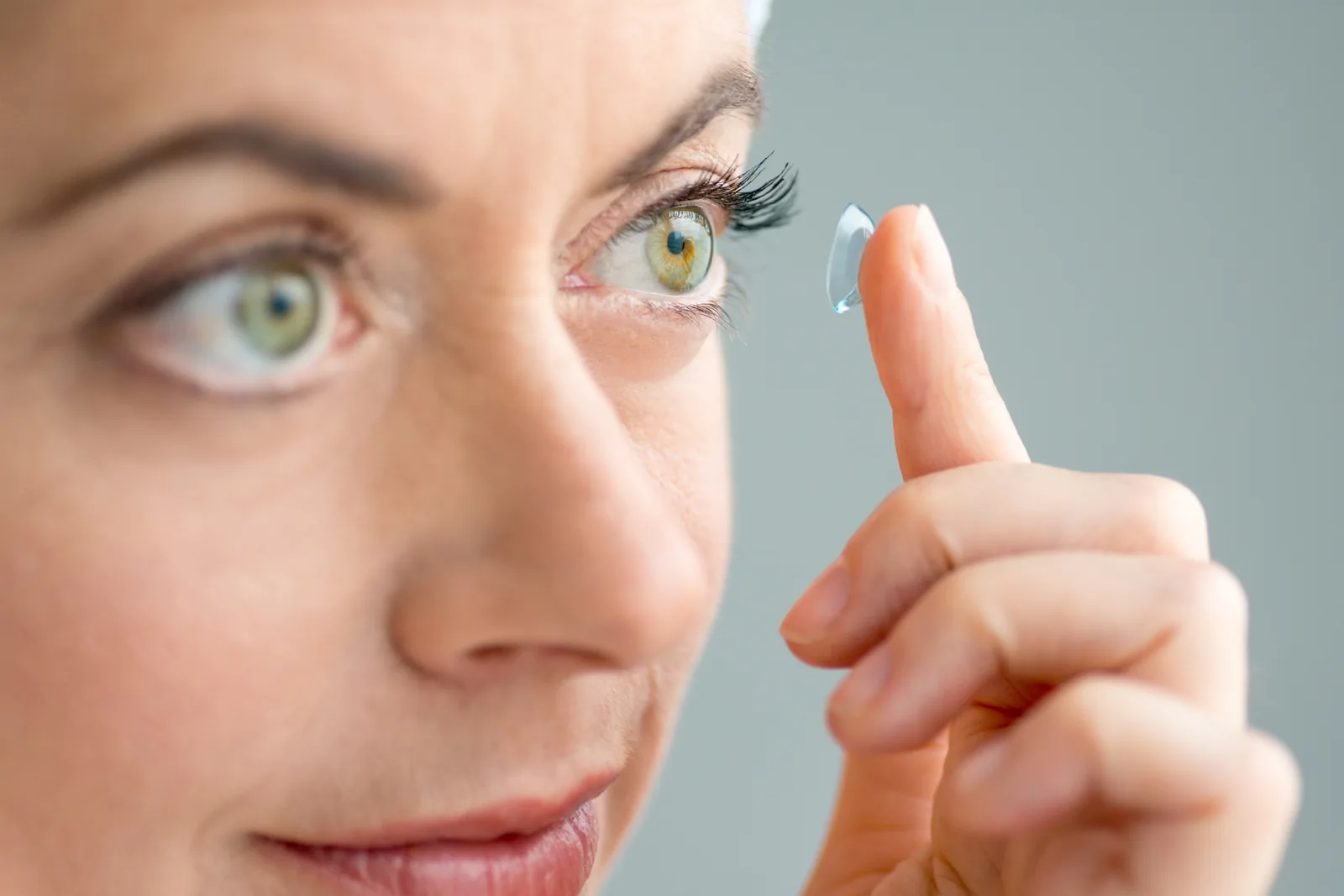 Vrouw houdt een contactlens op haar vingertop, klaar om in te zetten.