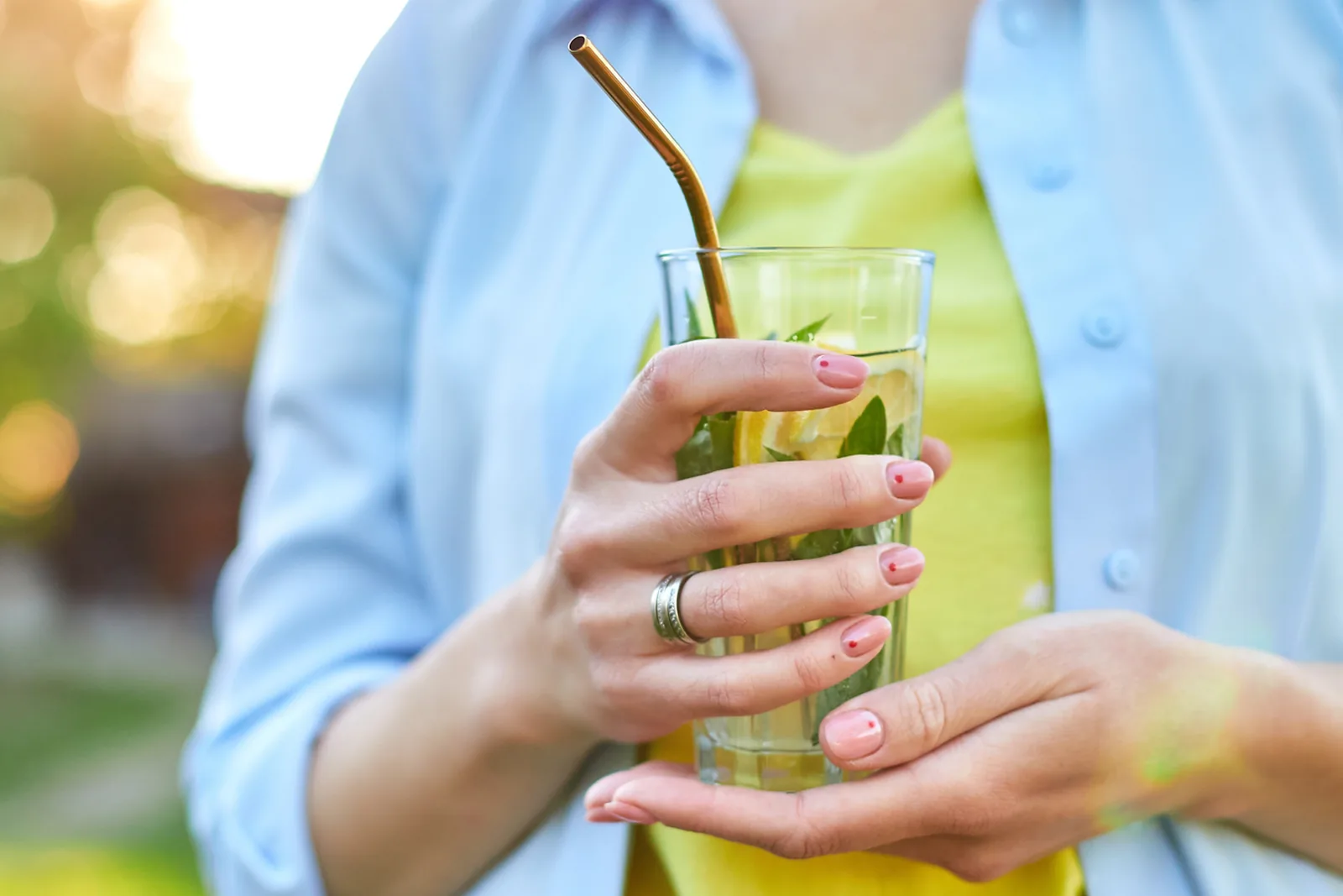 Vrouw houdt een glas limonade met een metalen rietje vast.