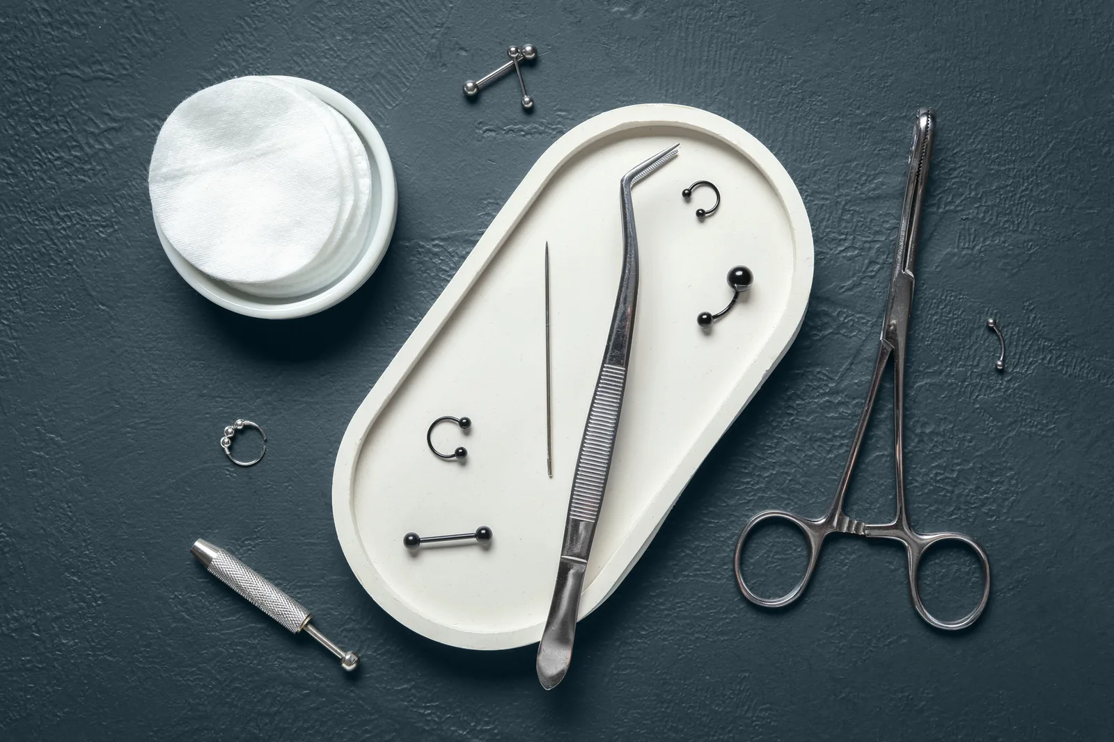 Piercingmateriaal en sieraden op een schaaltje: pincet, klem en naald.