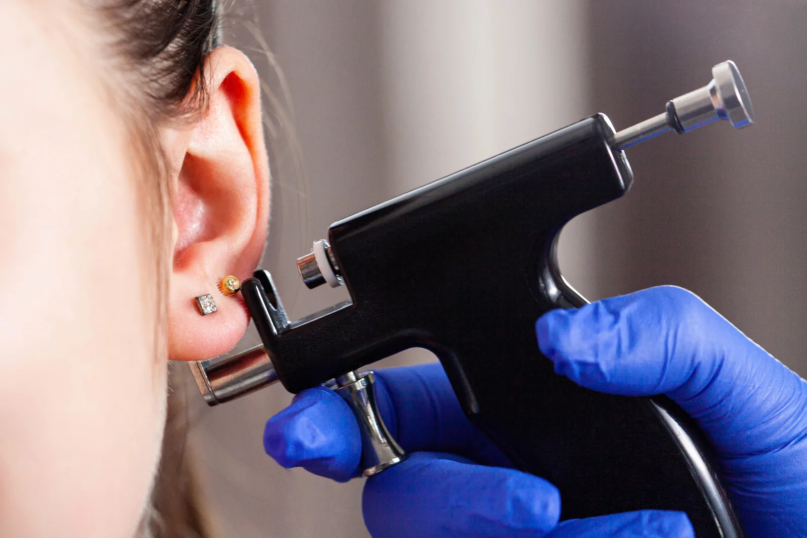 Specialist met blauwe handschoenen zet een oorlelpiercing.