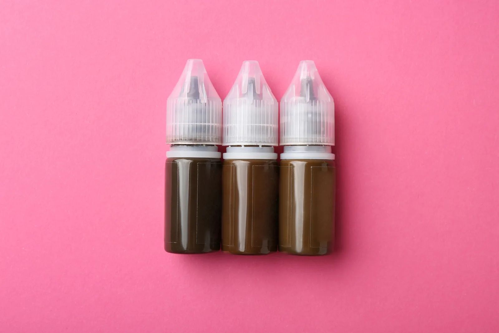 Drie flesjes bruin PMU-pigment op een roze achtergrond.