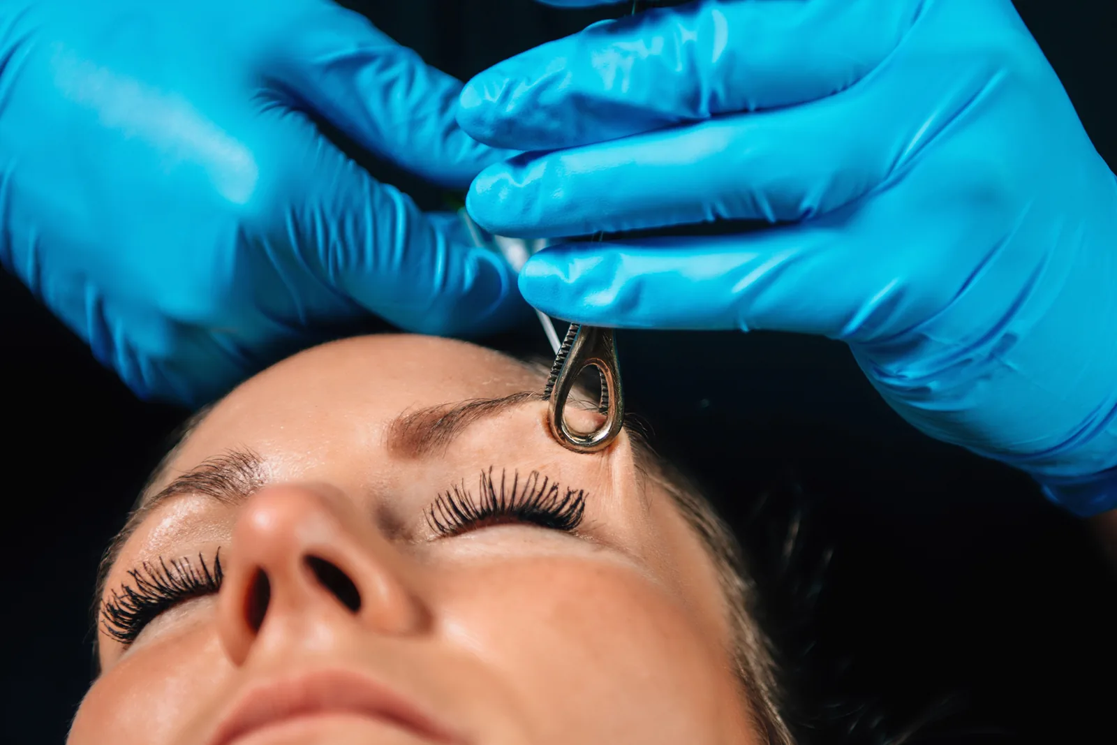 Piercer met blauwe handschoenen werkt bij een klant in de studio.