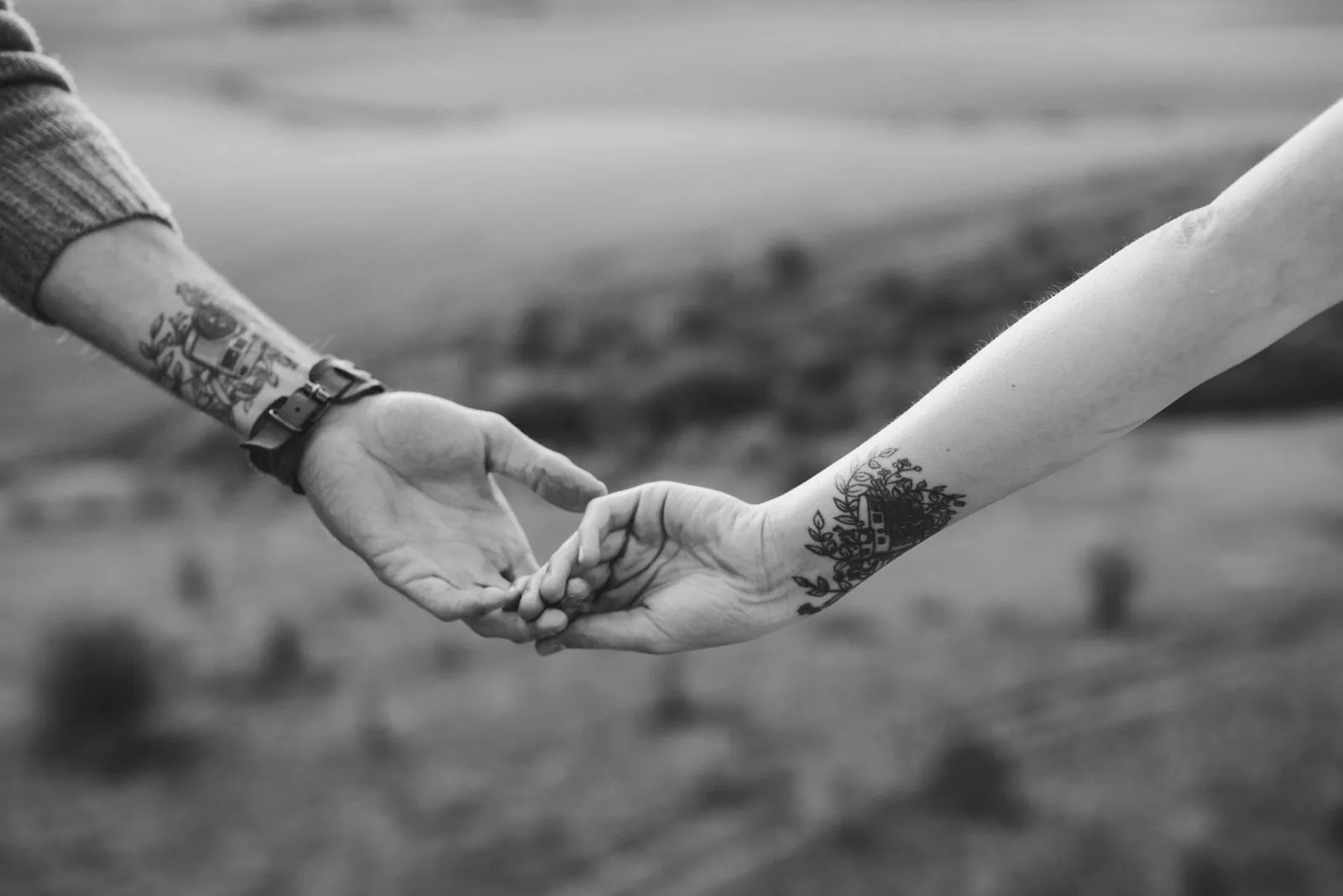 Een koppel houdt elkaars hand vast, allebei met een tattoo op de onderarm