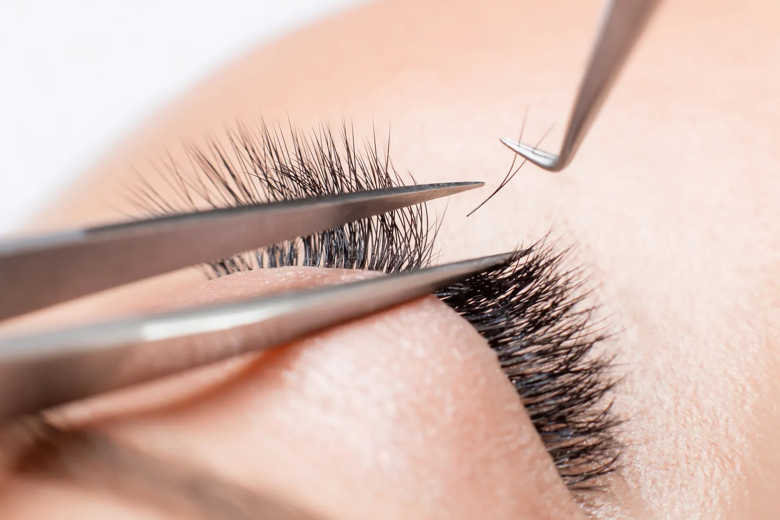 Stylist zet met een pincet wimperextensions op de eigen wimpers