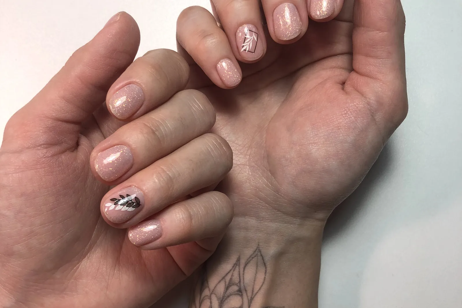 Twee handen met fijne tattoos en een bijpassende manicure